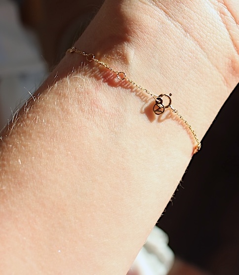 A close-up of a wrist with a delicate gold chain bracelet featuring a small charm shaped like a bicycle.