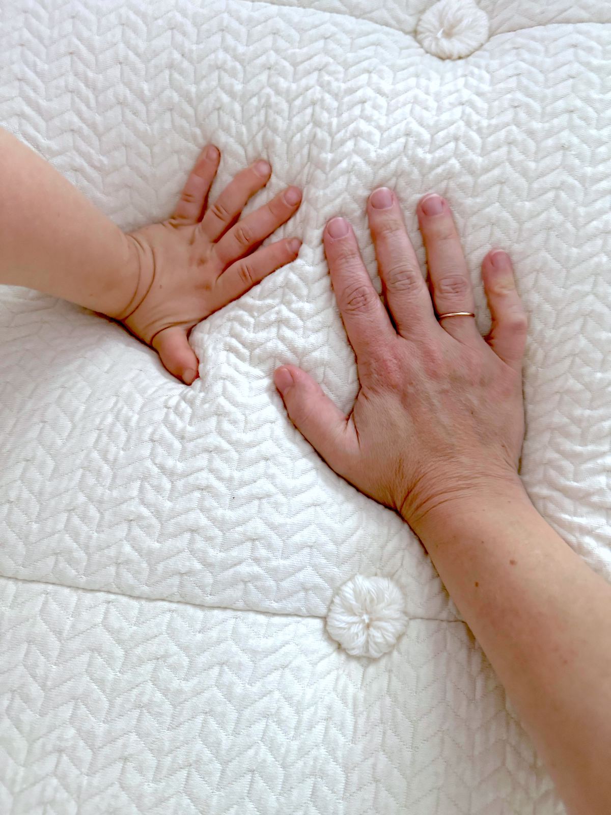 An adult hand and a child's hand press down on a white quilted surface, showcasing the comfort of an organic mattress.