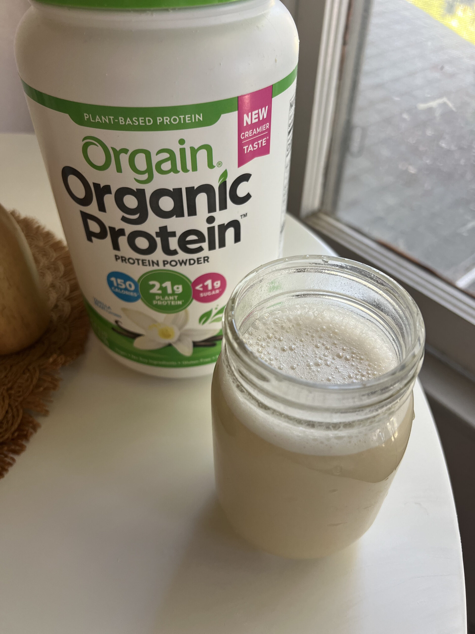 A jar of protein shake in front of a container of Orgain Organic Protein powder with vanilla flavor.