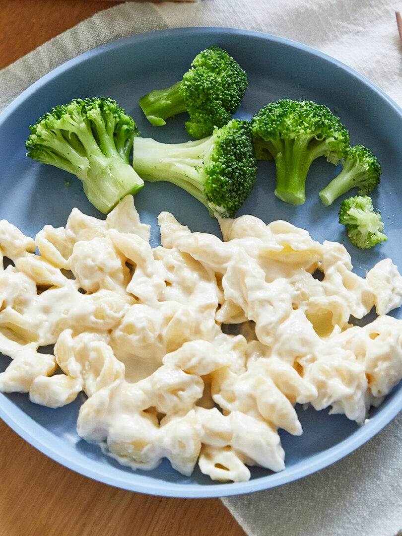 A blue plate containing macaroni and cheese next to steamed broccoli florets.