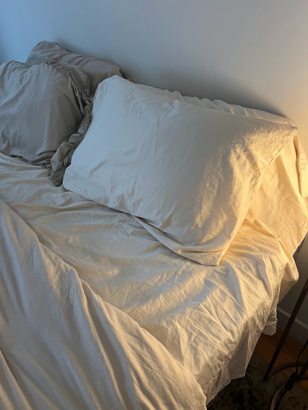 A neatly made bed with light-colored sheets and pillows, beside a lit lamp on a nightstand.