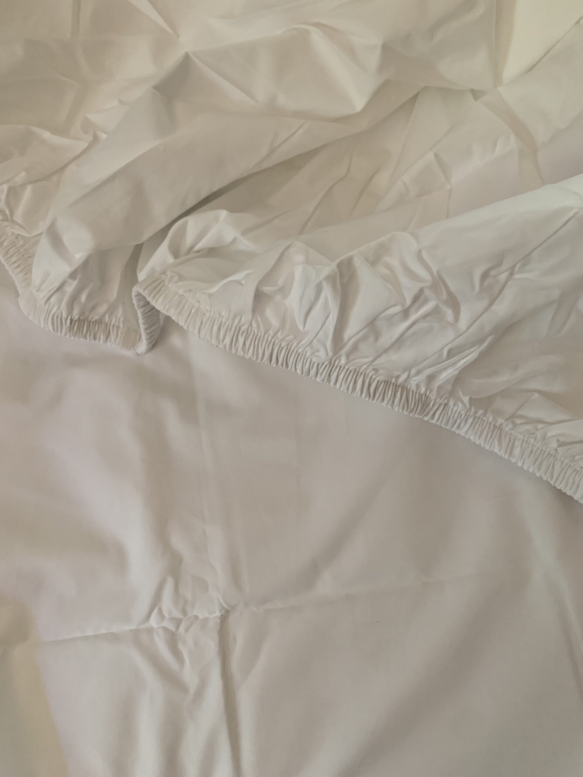 A crumpled white fitted sheet partially laid over a smooth bed surface.