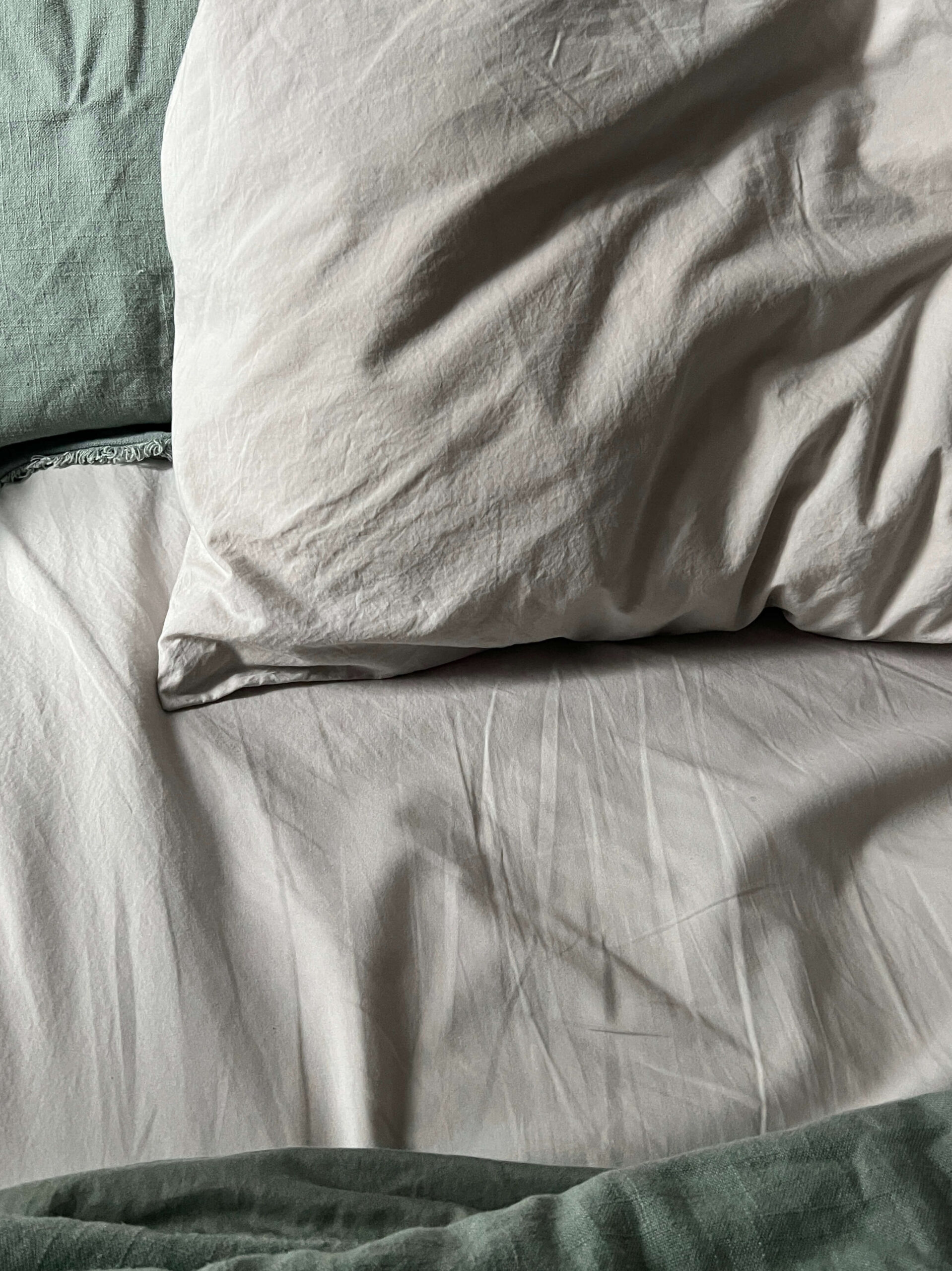 Close-up of an unmade bed with white pillows and green sheets, showing visible creases and folds.