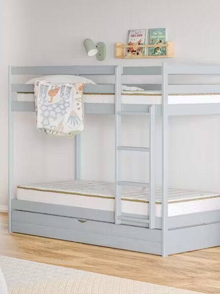 A light gray bunk bed with a ladder and storage drawer underneath is situated in a bedroom with white walls, wooden floors, and various children’s decor items and furniture.