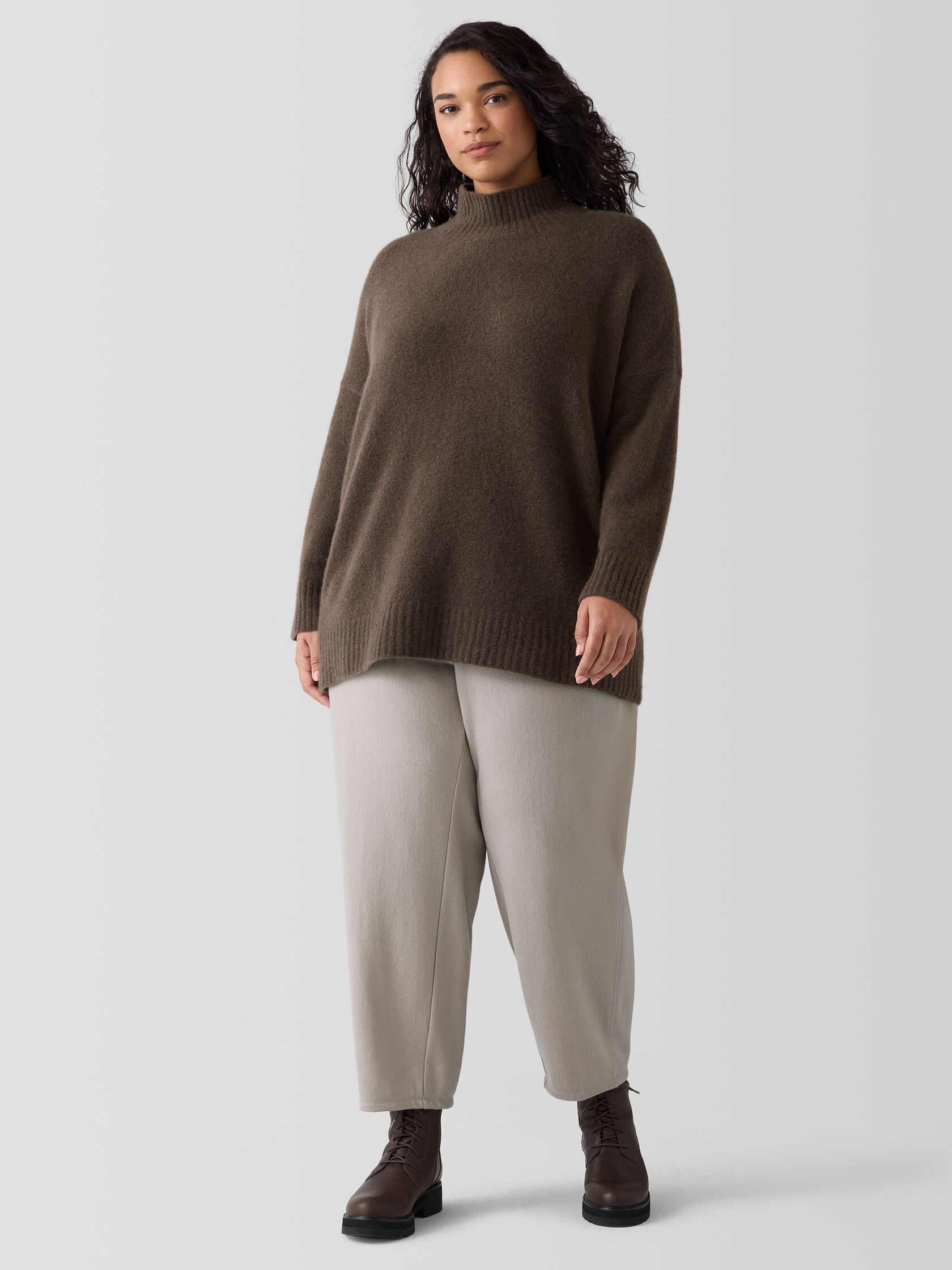 A plus size model wearing a brown turtleneck and grey pants from Eileen Fisher. 