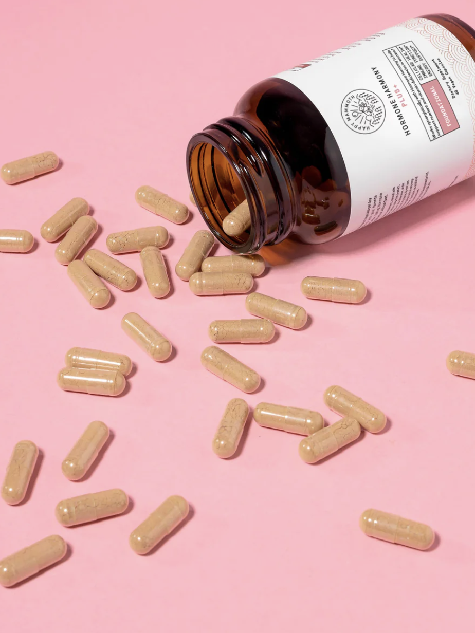 A brown bottle of supplements lies on its side, spilling beige capsules onto a pink surface.