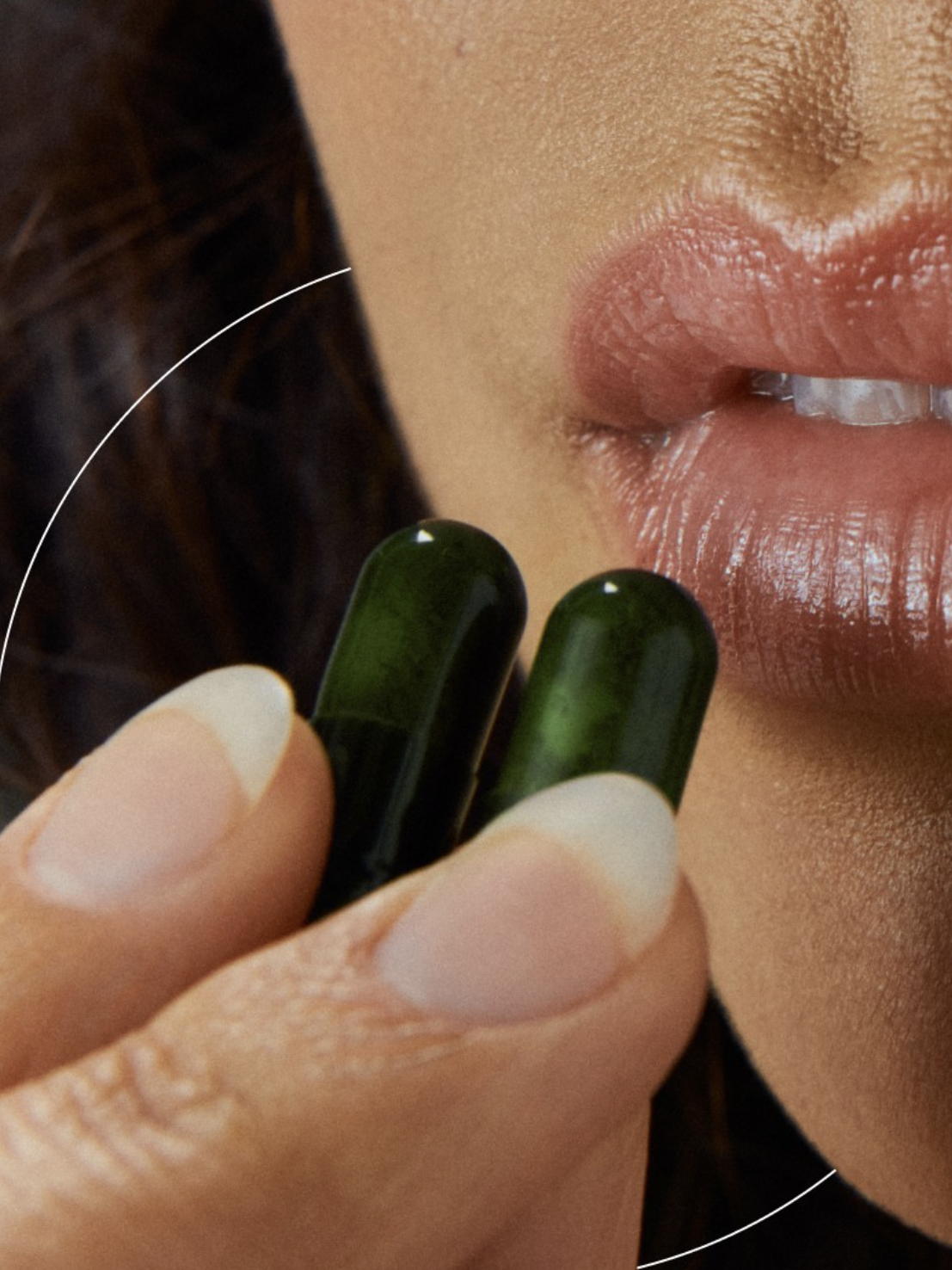 Close-up of a person's mouth and hand holding two green capsules near their lips.