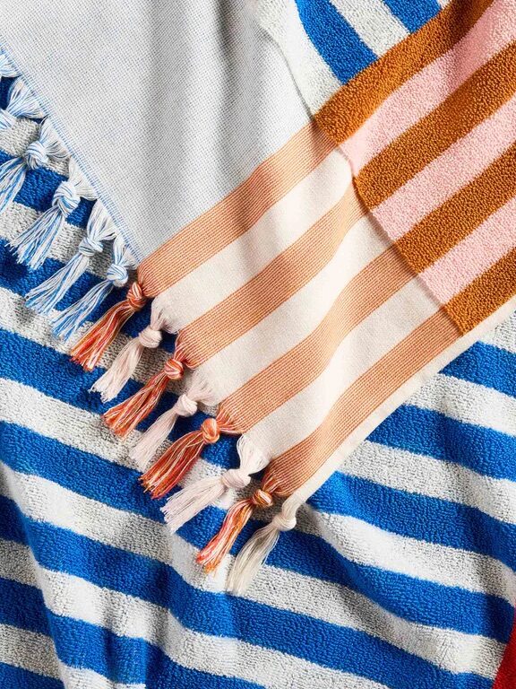 Variety of striped fabrics in blue, white, brown, pink, and orange, layered diagonally, each with tassel details at the ends.