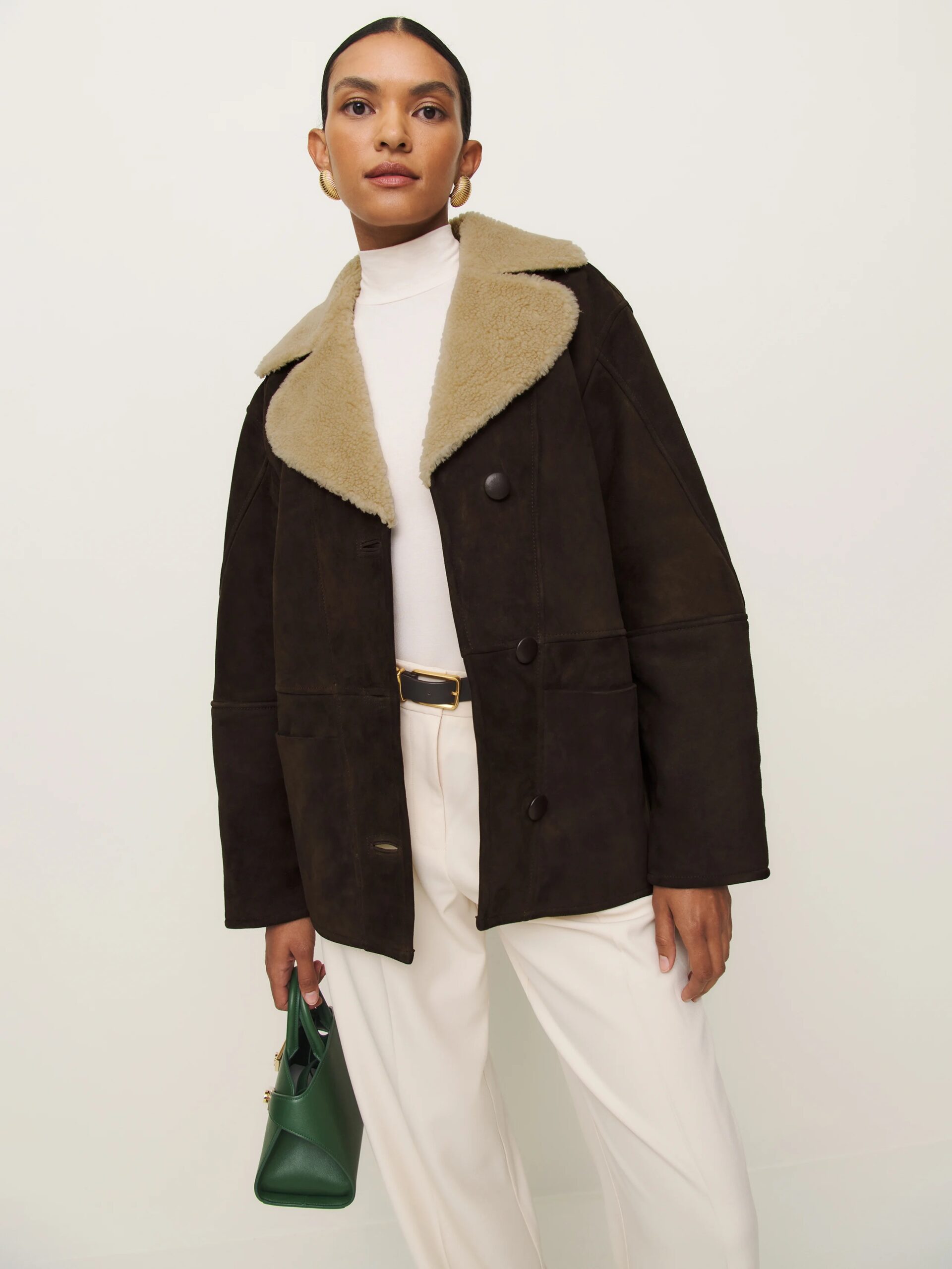 A model wearing a brown oversized suede jacket with a beige fur collared trim from Reformation. 