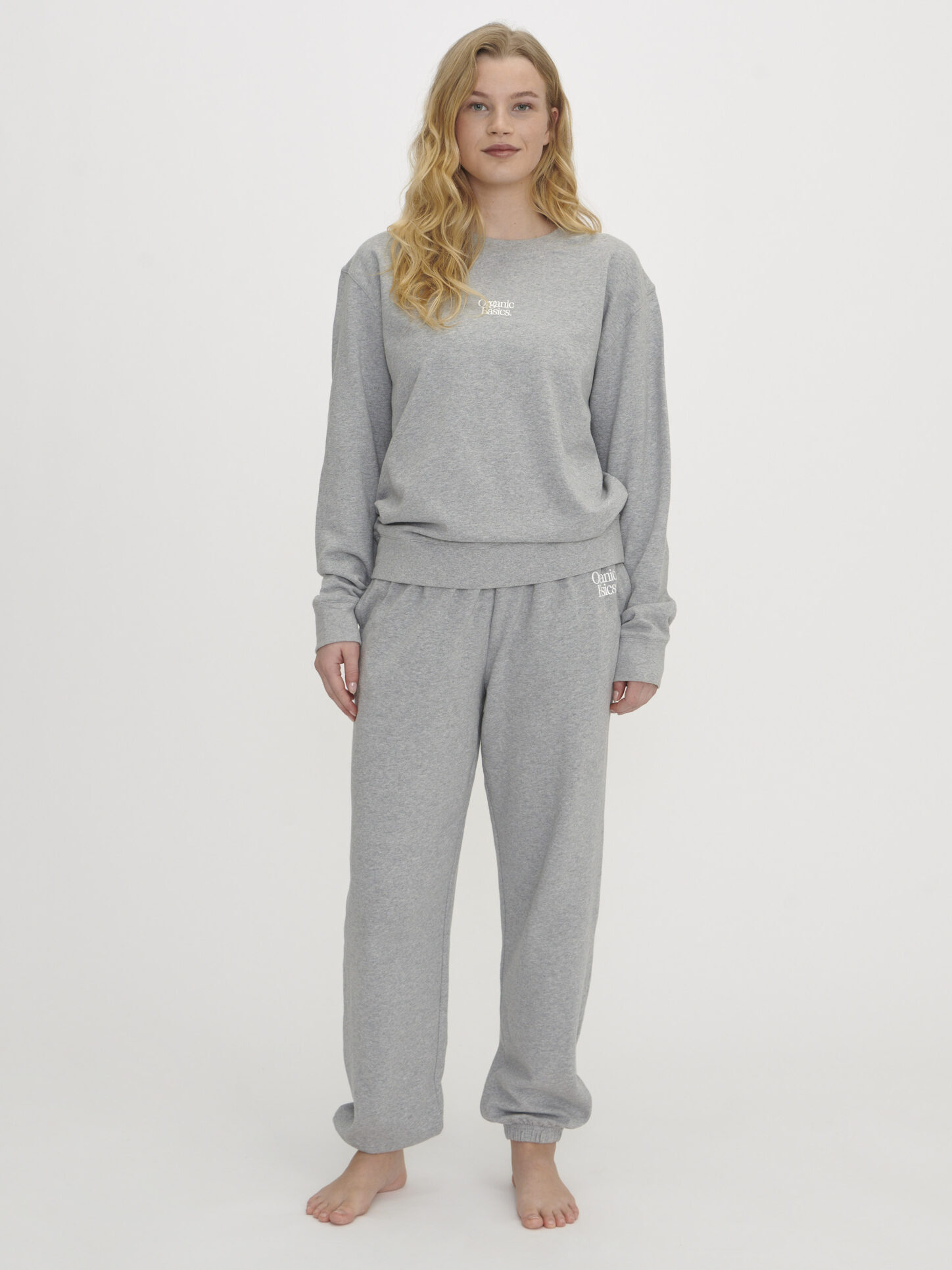 Person standing barefoot against a white background, dressed in a grey sweatshirt and matching sweatpants.