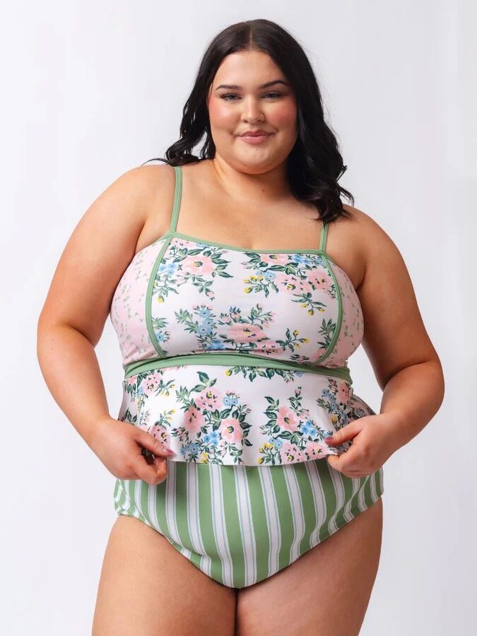 A woman wearing a floral and striped swimsuit against a plain background.