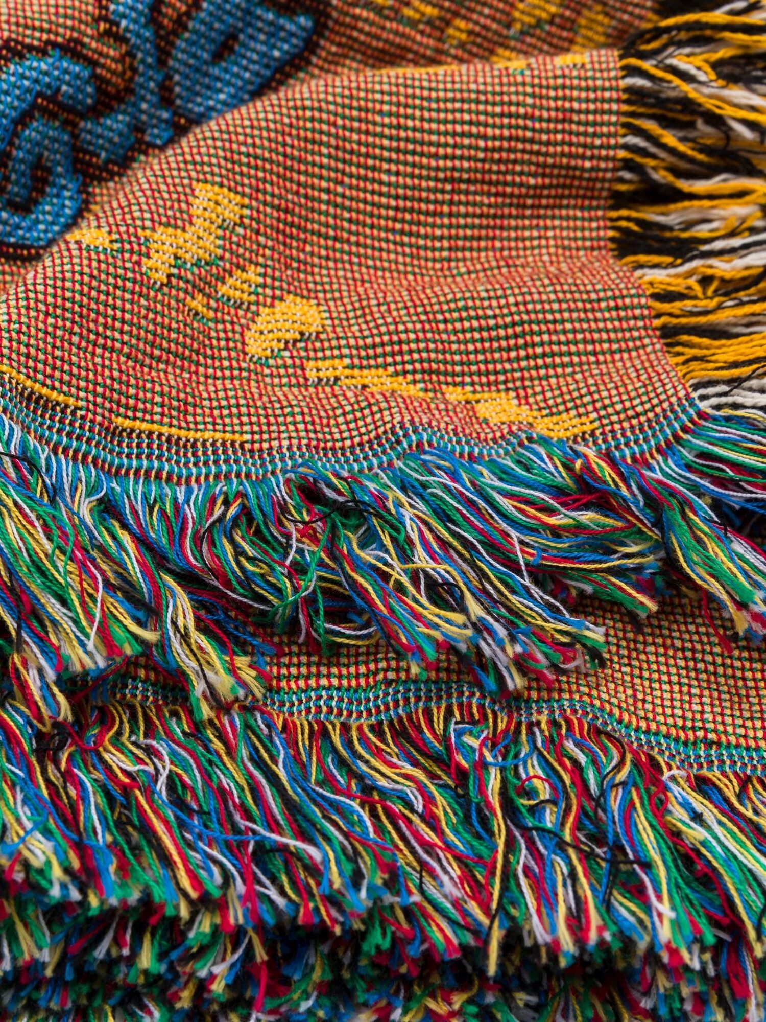 Close-up of colorful woven fabric with intricate patterns and hanging fringes in shades of blue, yellow, green, and red.