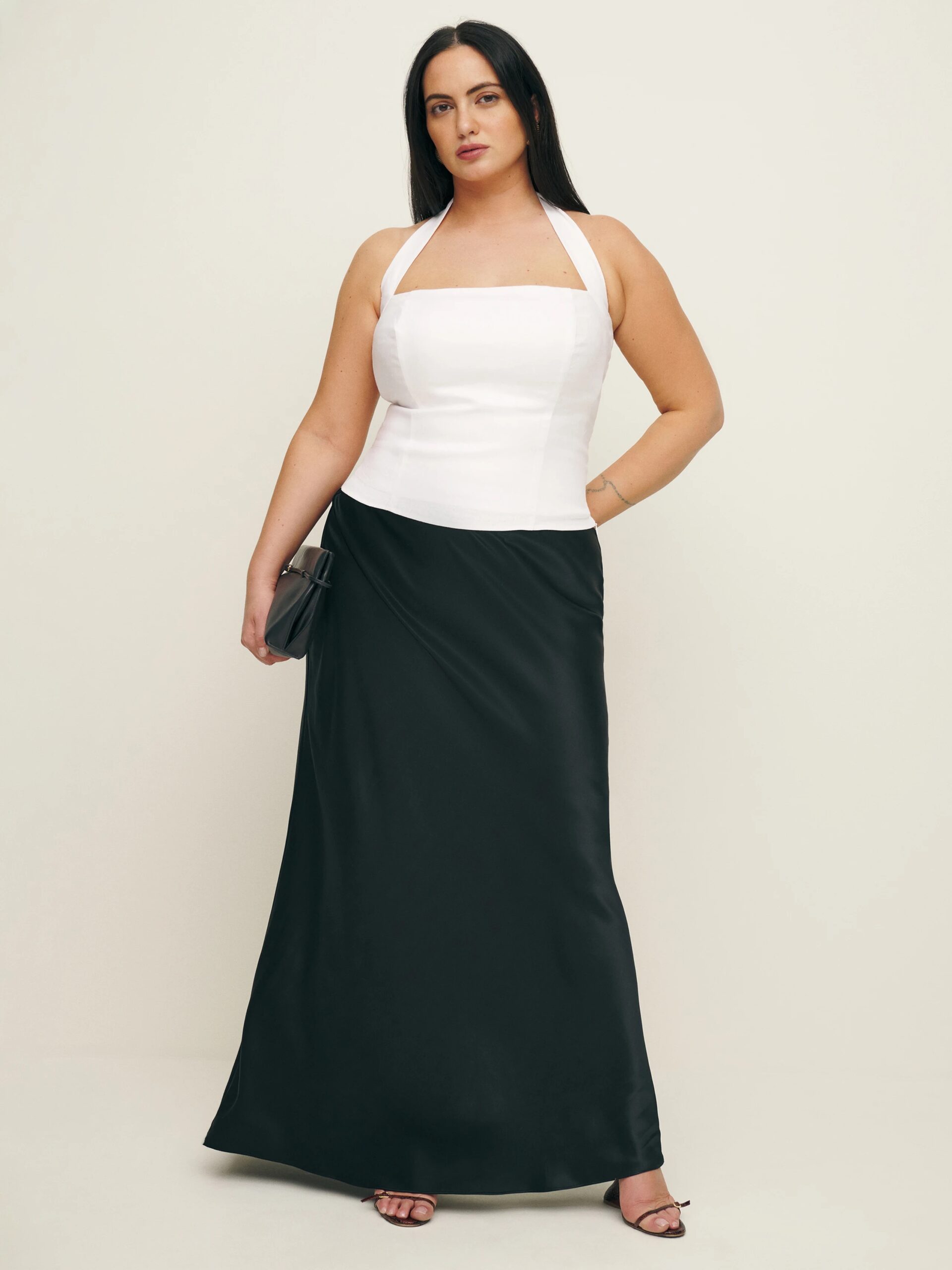 A plus size model wearing a white halter top and a black silk skirt from Reformation. 