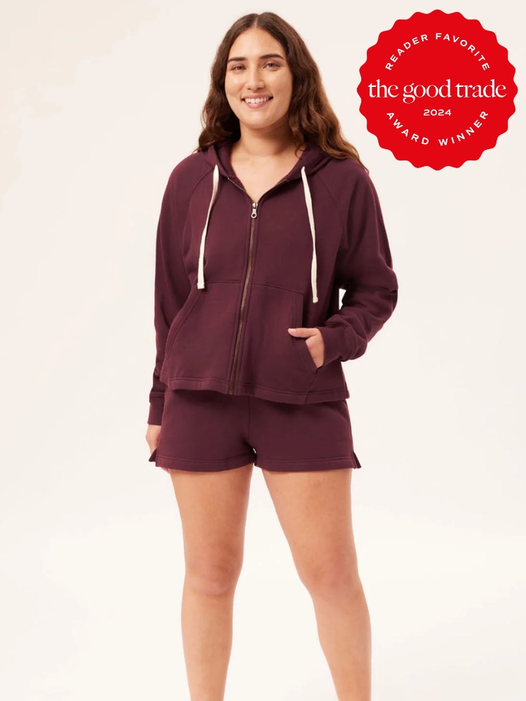 Person wearing a matching burgundy hoodie and shorts set, smiling, with a red award badge in the top-right corner reading "The Good Trade 2024 Reader Favorite Award Winner.