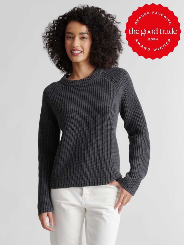 A person with curly hair wears a charcoal grey sweater and white pants, smiling. A red badge on the top right reads "Reader Favorite The Good Trade Award Winner 2024.