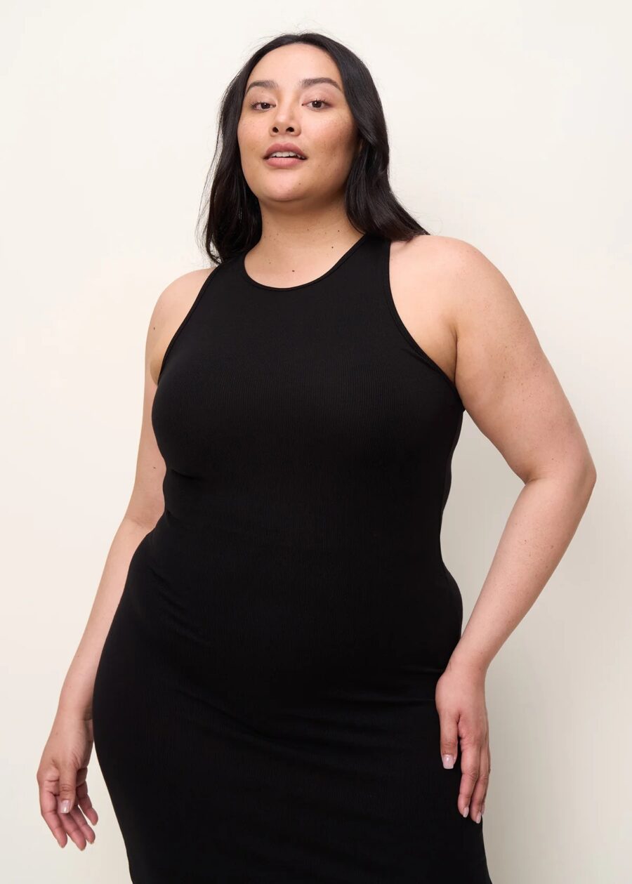 A plus size model wearing a black racerback tank dress from The Standard Stitch.