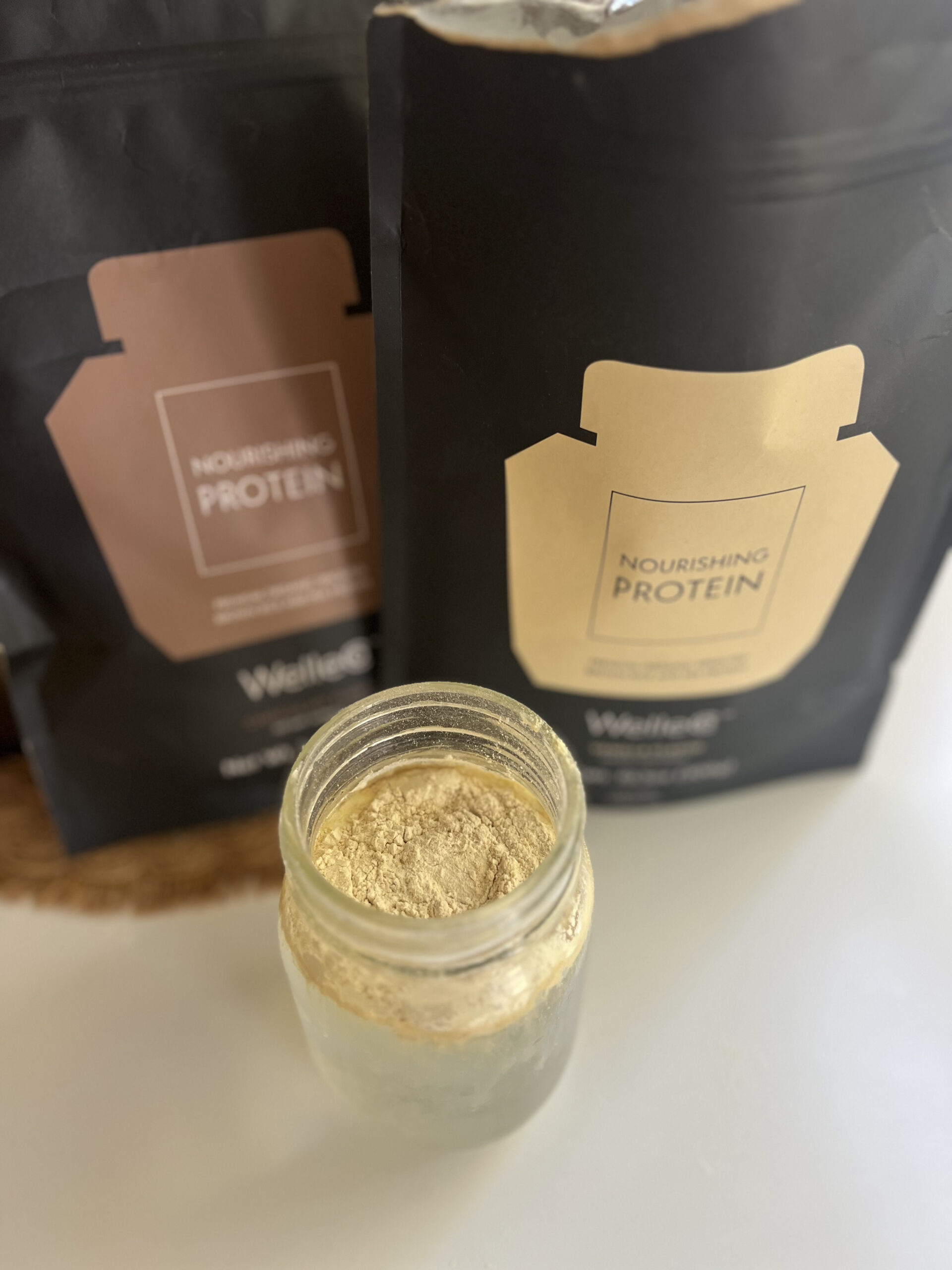 Two bags of nourishing protein powder are next to a glass jar filled with the powder.