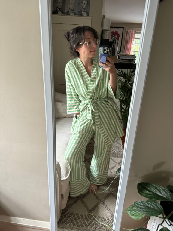 A woman with dark hair wears a top and bottom pajama set that is green and white striped, with a tie around the top.