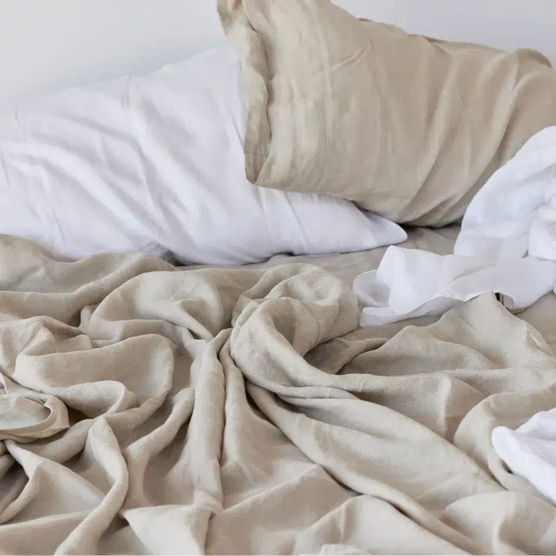 Unmade bed with beige sheets and white pillows.