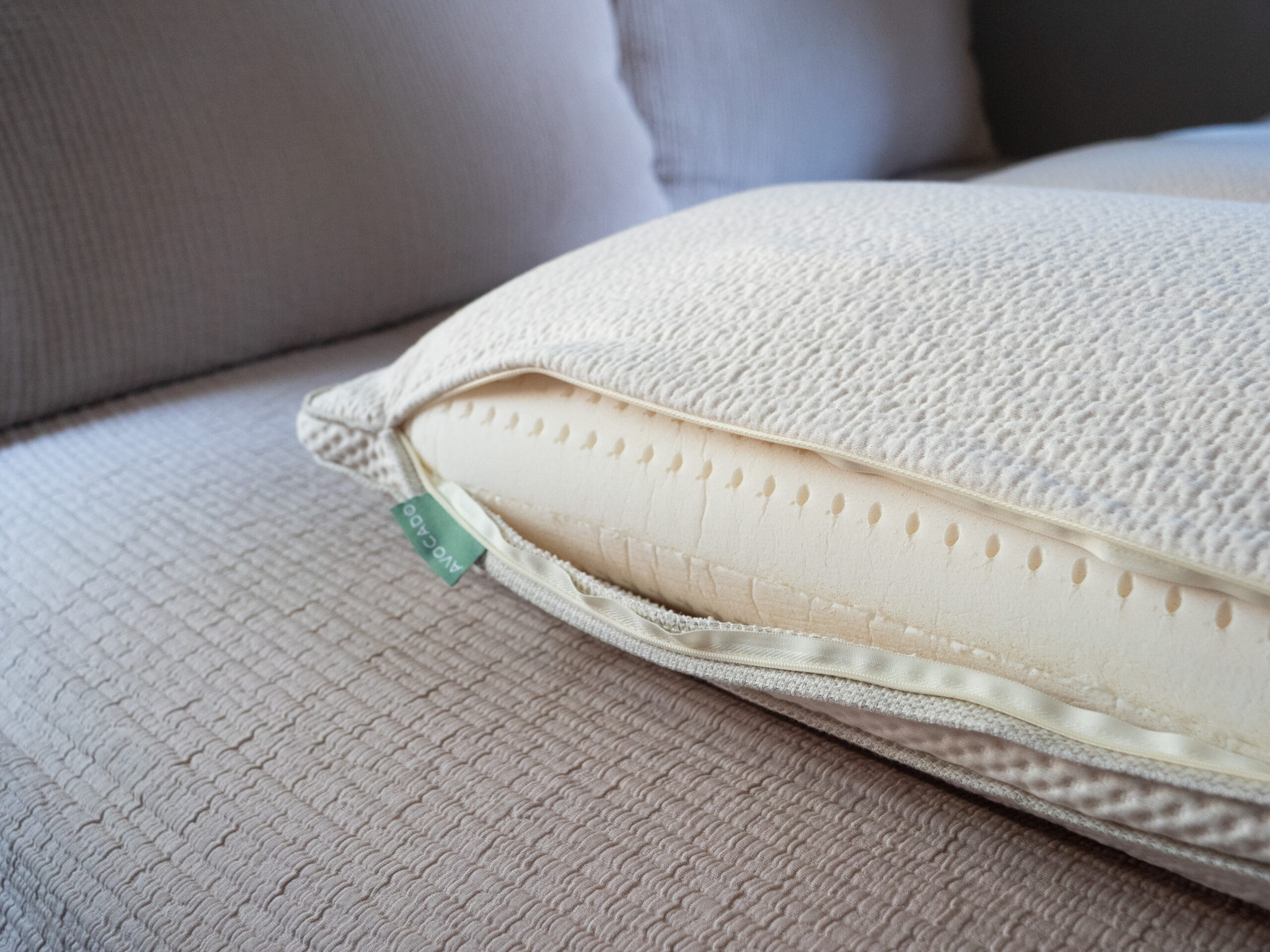 Close-up of a partially unzipped pillow with a visible inner foam layer, placed on a textured beige couch.