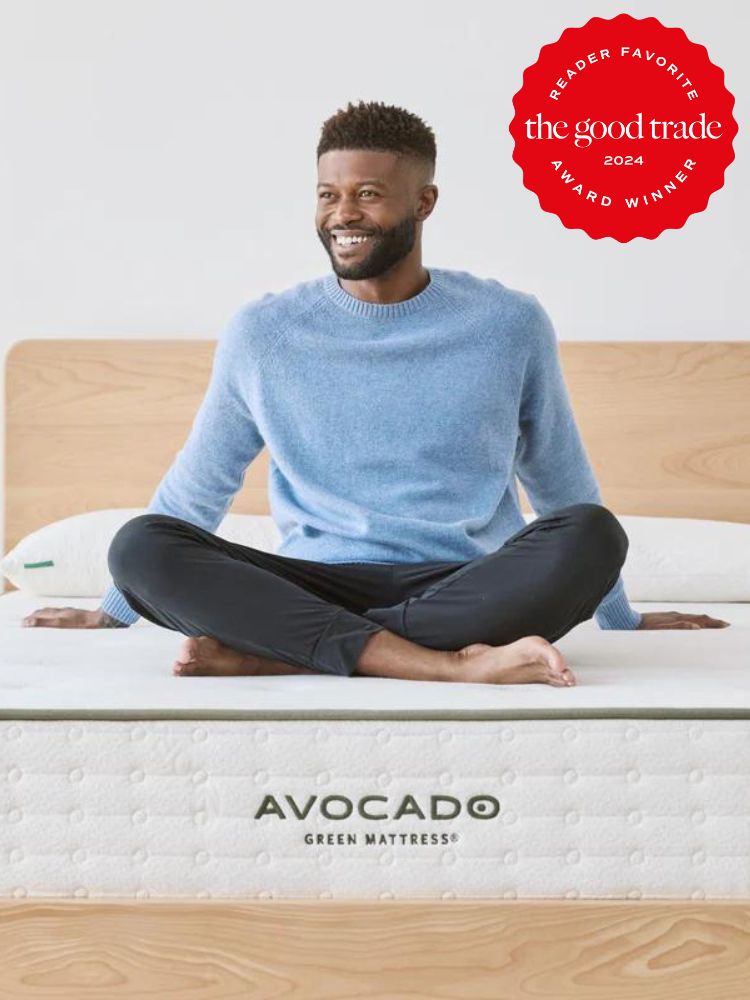 A smiling man sits cross legged on an Avocado Green Mattress that does not have blankets yet on it.