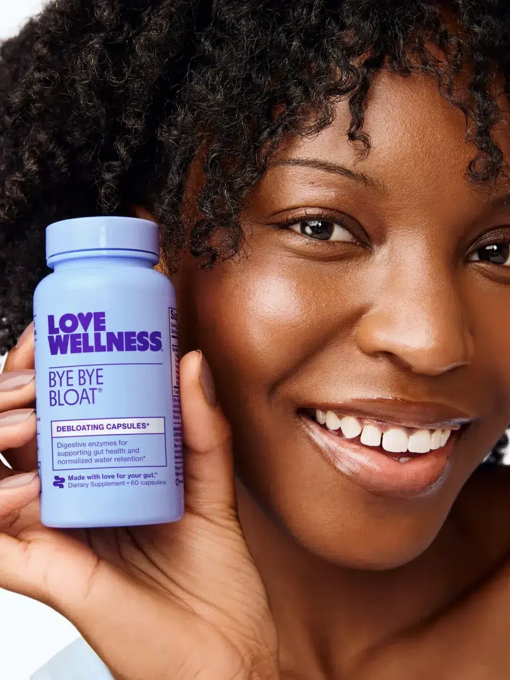 A person holds a bottle of Love Wellness Bye Bye Bloat debloating capsules close to their face, smiling.