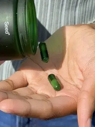 Person holding two green capsules in their palm, with a dark green container labeled "Seed" above the capsules.