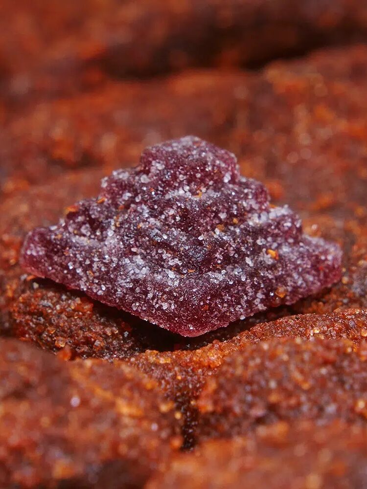 Close-up of a sugar-coated pyramid-shaped candy, surrounded by reddish-brown candies.