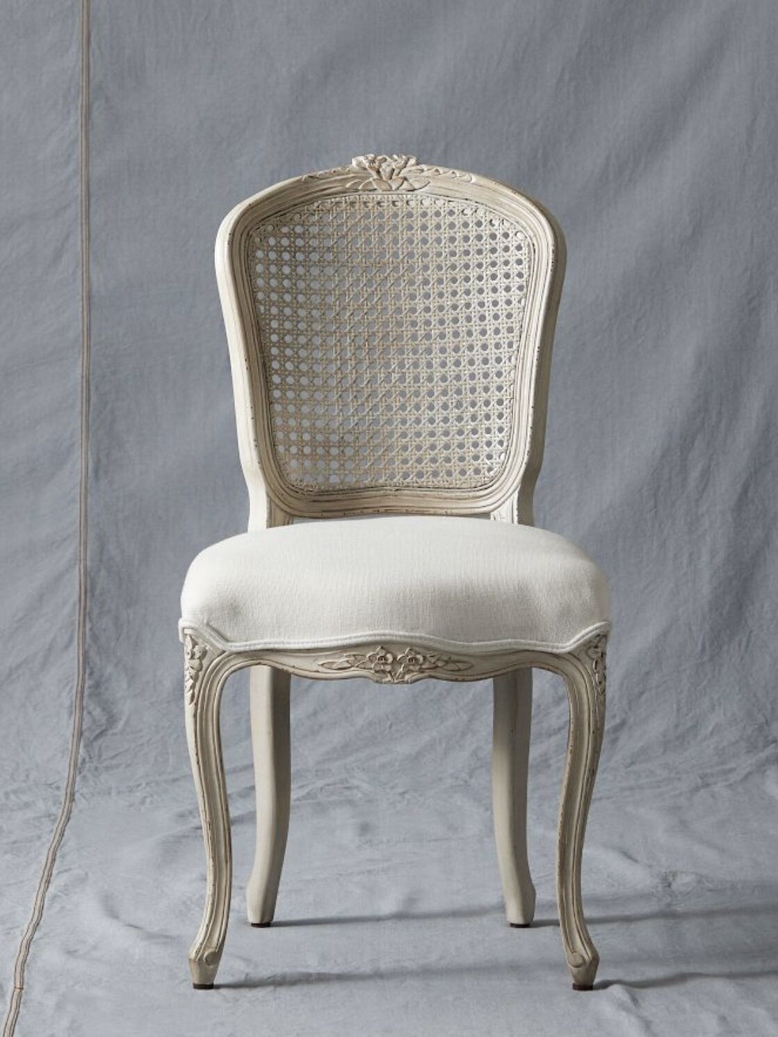 Elegant wooden chair with a woven backrest and cushioned seat, featuring ornate carvings, placed against a gray fabric backdrop.