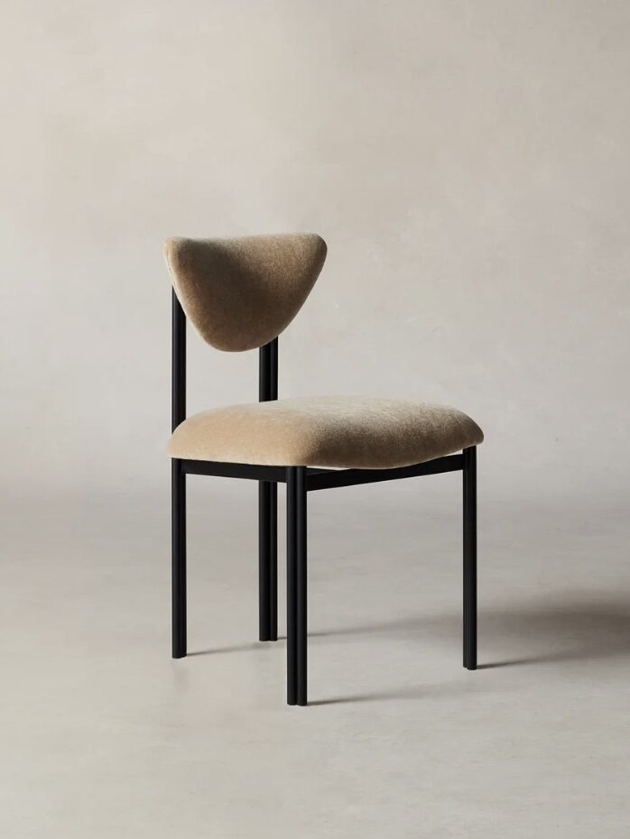 A minimalist chair with a black metal frame, light brown upholstered seat and backrest, positioned against a plain background.