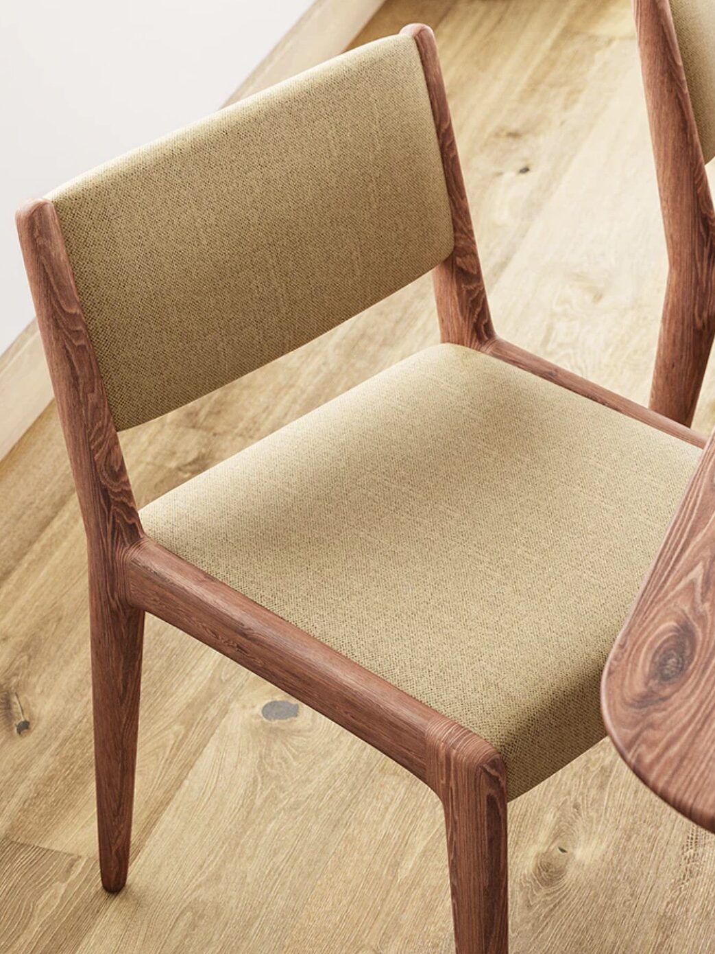 A wooden chair with beige fabric upholstery on the seat and backrest placed on a wooden floor.