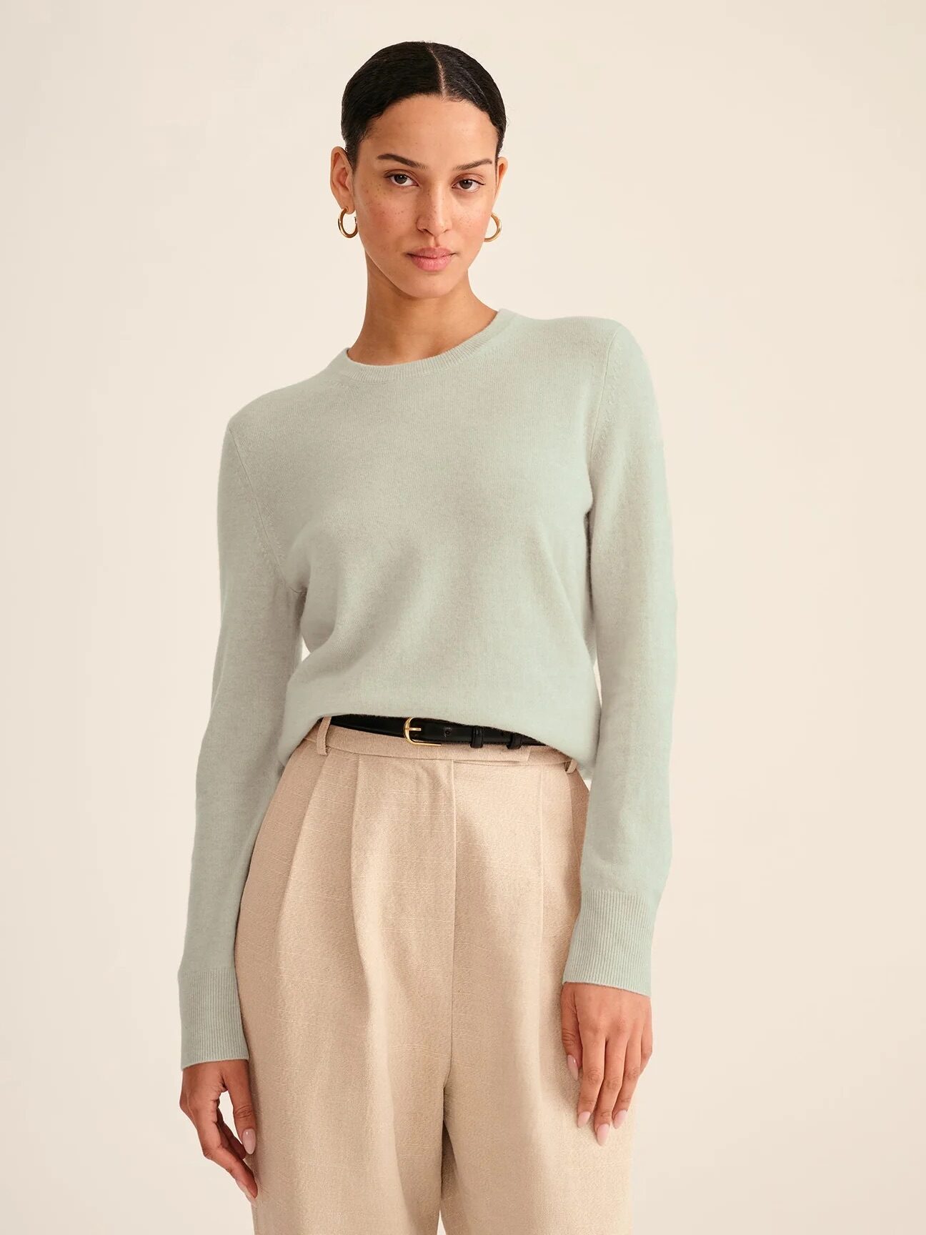 A model wearing a NAADAM cashmere sweater in a pale green. 