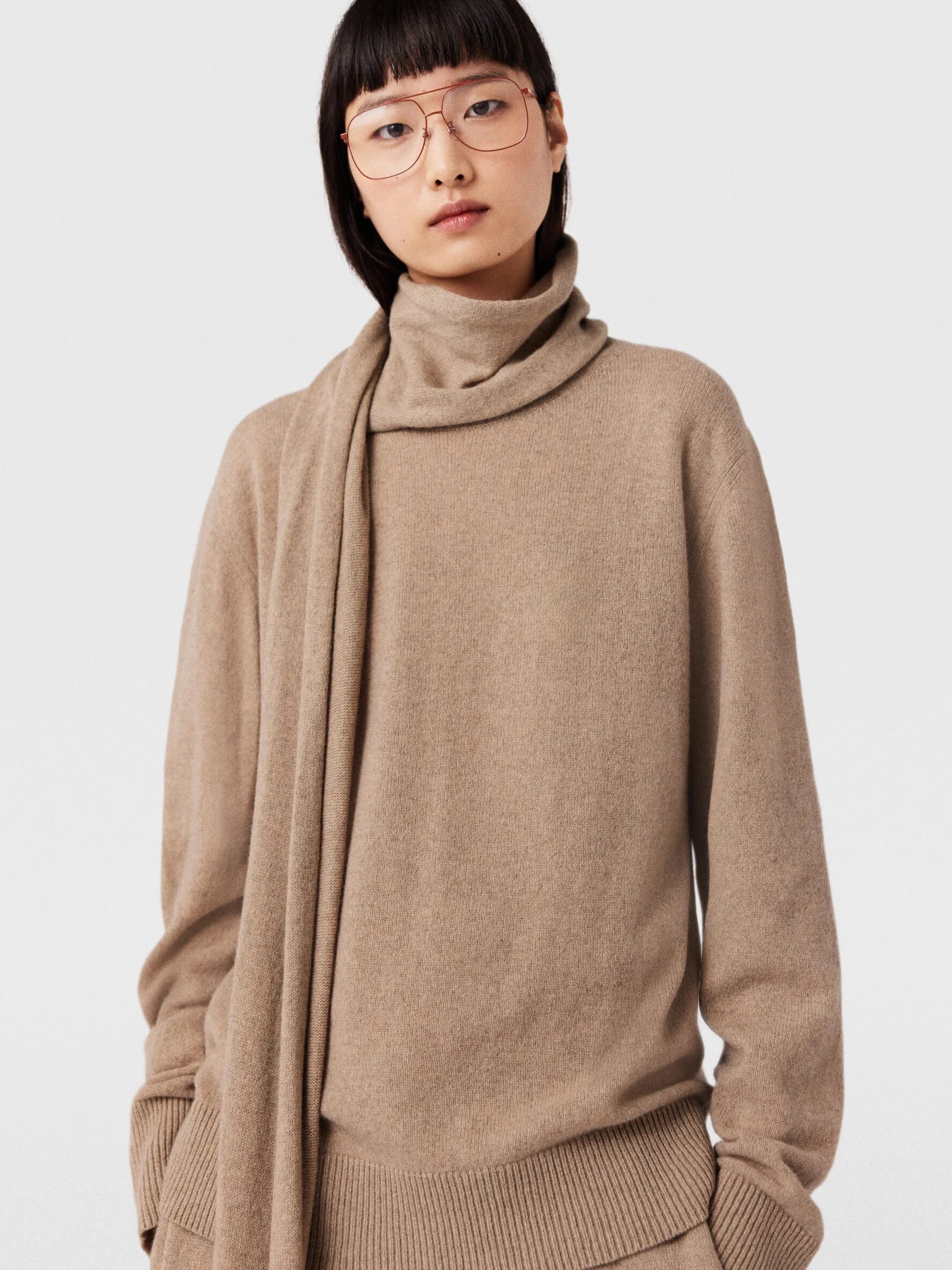 A model wearing a beige cashmere turtleneck with an attached scarf from Stella McCartney. 