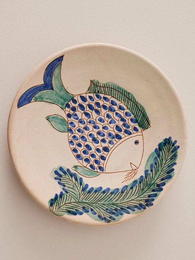 Ceramic plate with hand-painted blue and green fish design, surrounded by green foliage pattern.