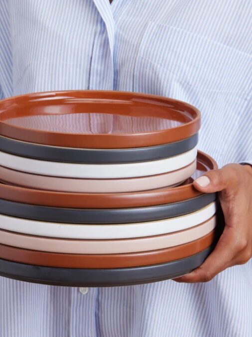 Person in a striped shirt holding a stack of four ceramic dishes with brown, white, and black stripes.