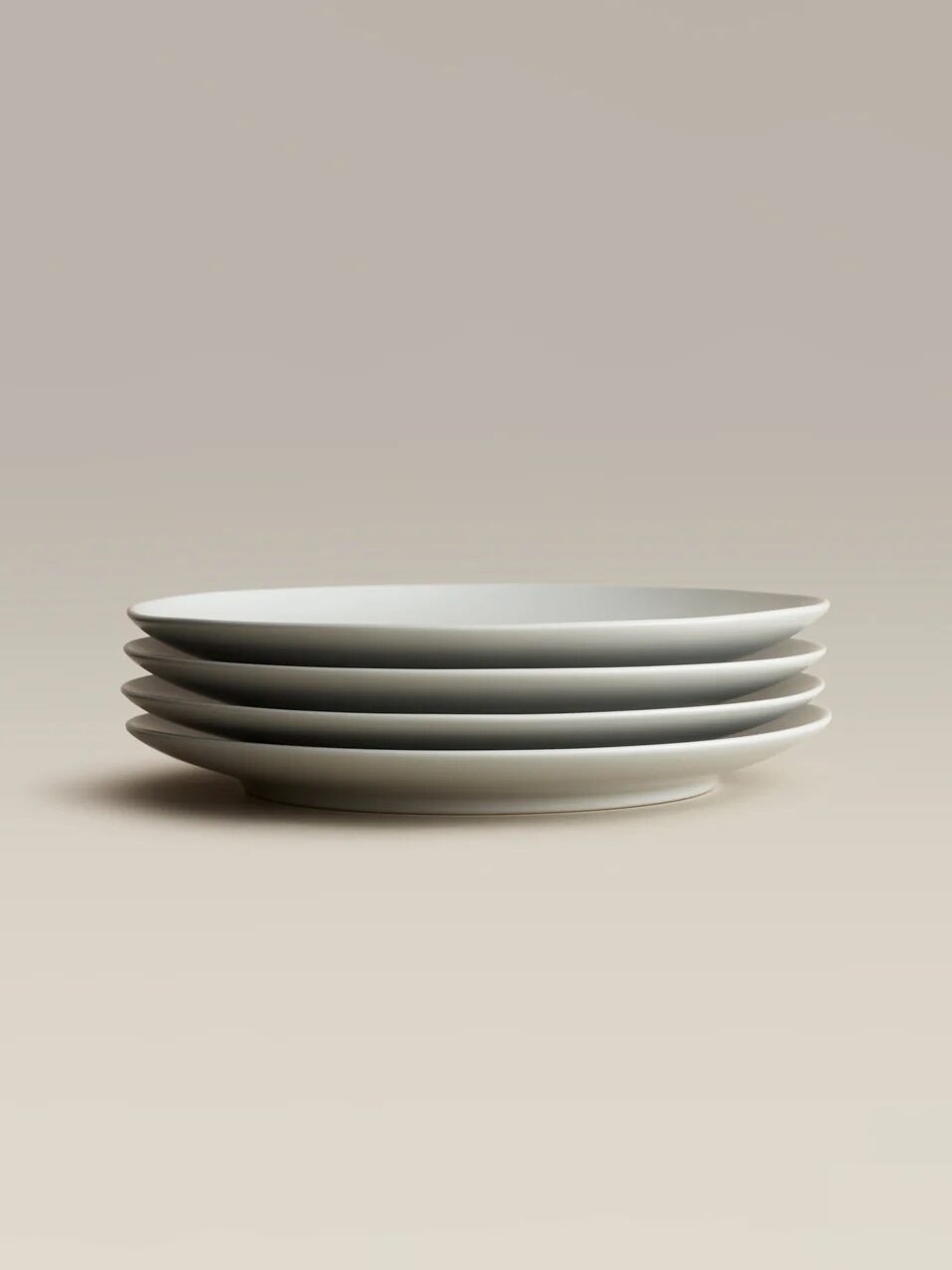 A stack of four white ceramic plates placed against a neutral background.