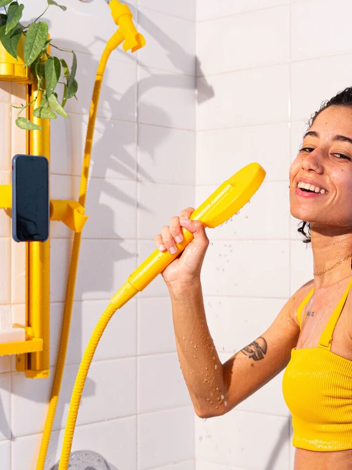 A model holding up a running sproos! shower head in yellow. 