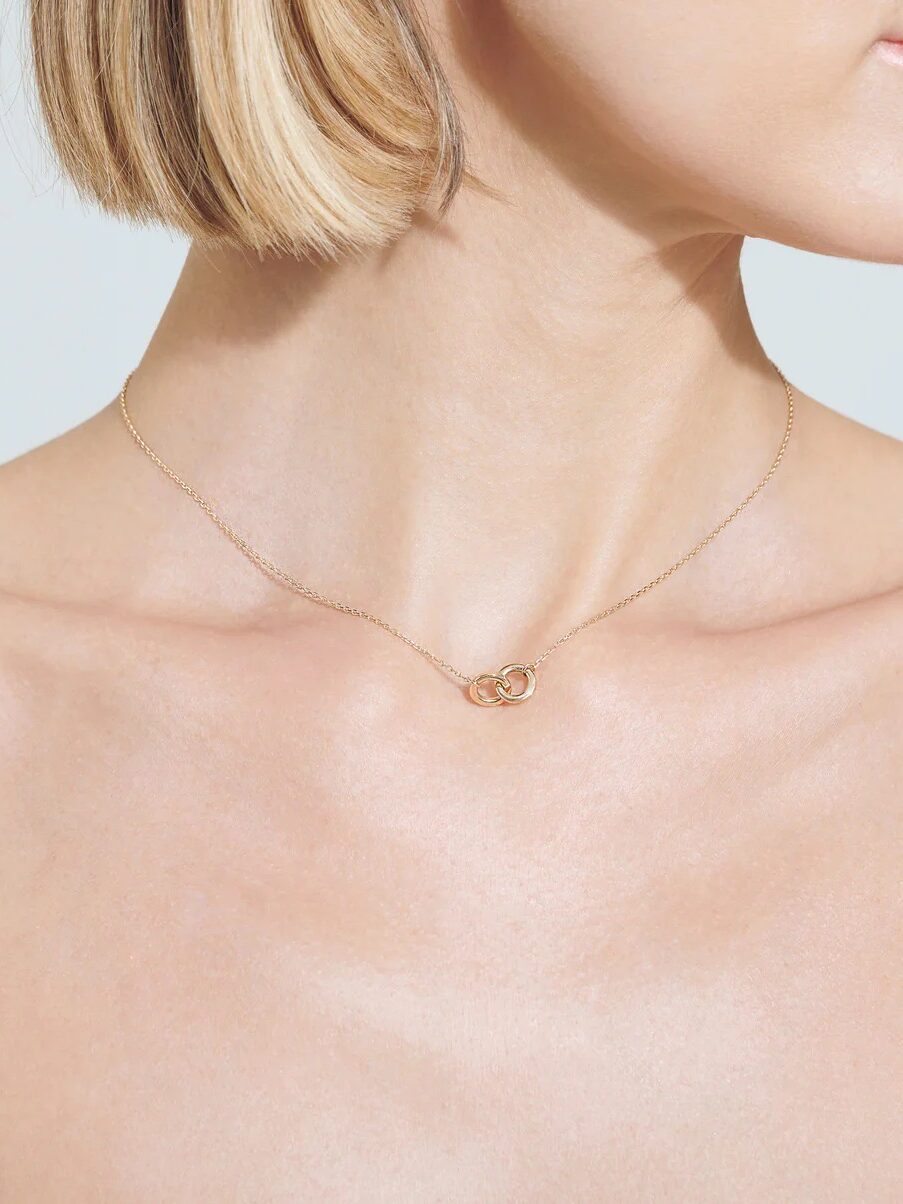 A close up of a model wearing a gold pendant necklace with two interlinking hoops from Aurate. 