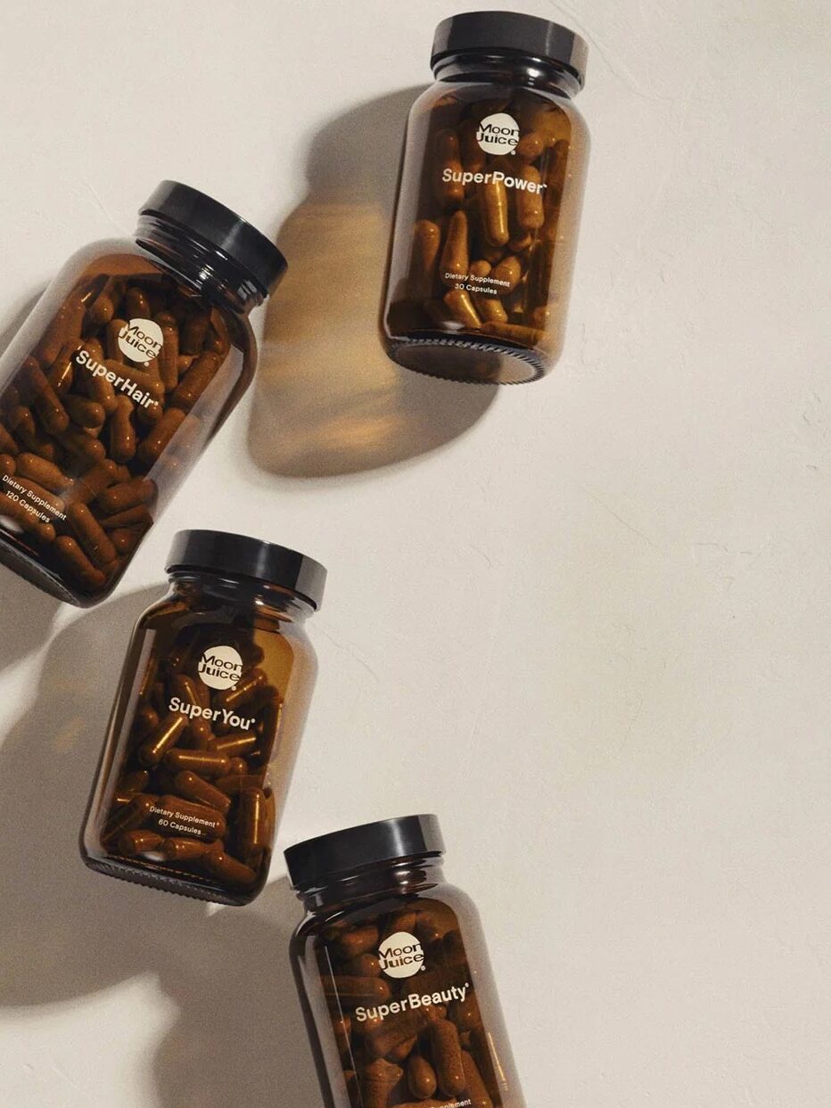 Four brown glass bottles with black caps, filled with capsules, arranged diagonally on a beige surface. The labels read "Quality Mushrooms.