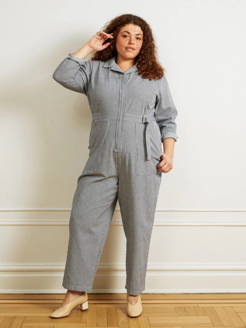 A plus size model wearing a grey pinstripe jumpsuit from Loup. 