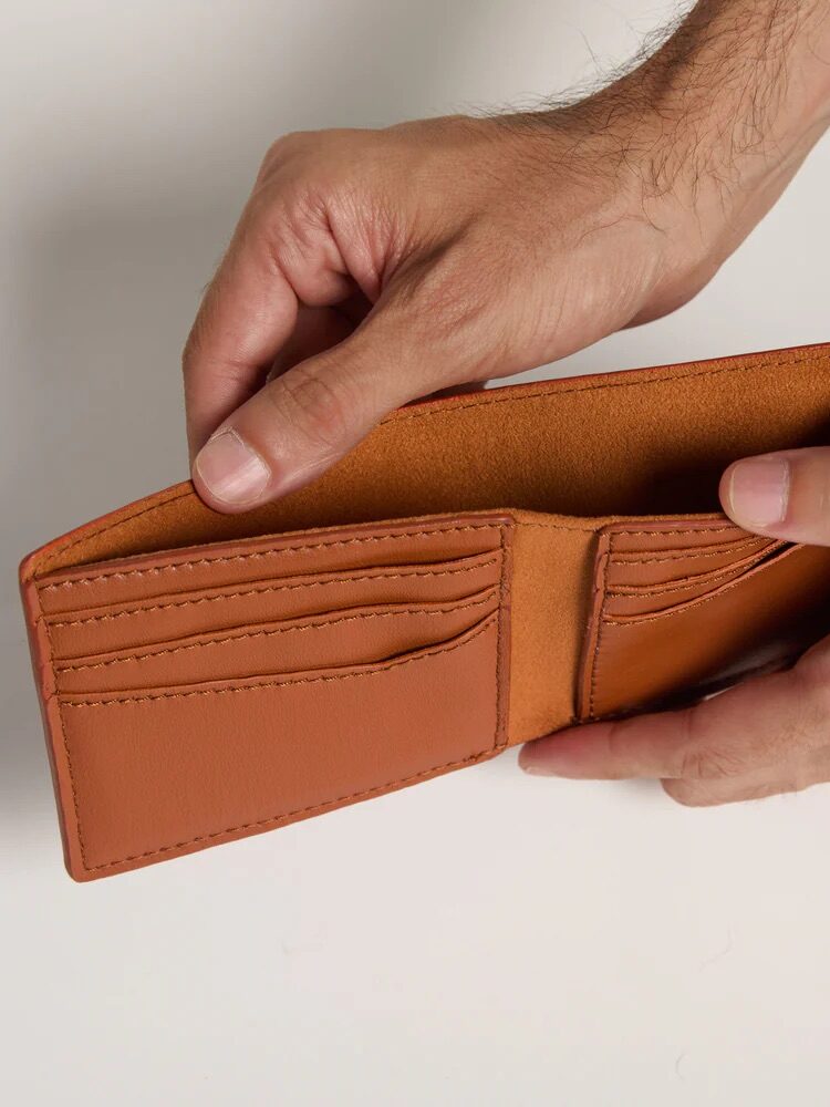 A pair of hands opening up a tan wallet from Allegorie. 