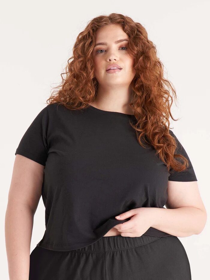 A plus size model wearing a black crop t-shirt from The Standard Stitch. 