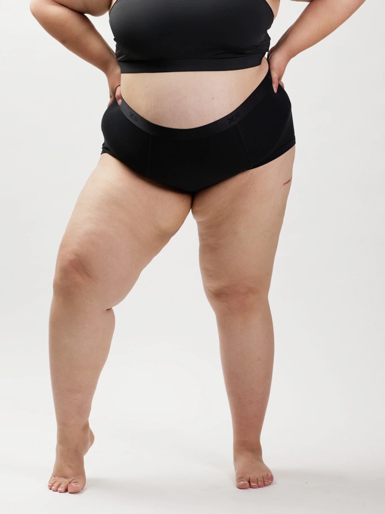 A plus size model wearing a TomboyX bralette and boxer briefs set. 