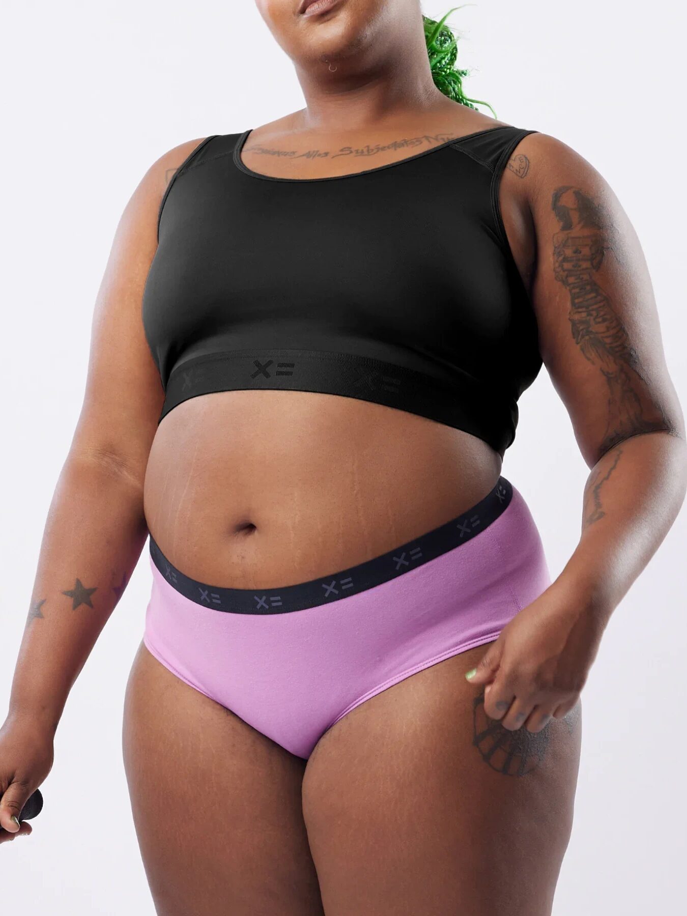 A plus size model wearing a TomboyX bralette and briefs set. 