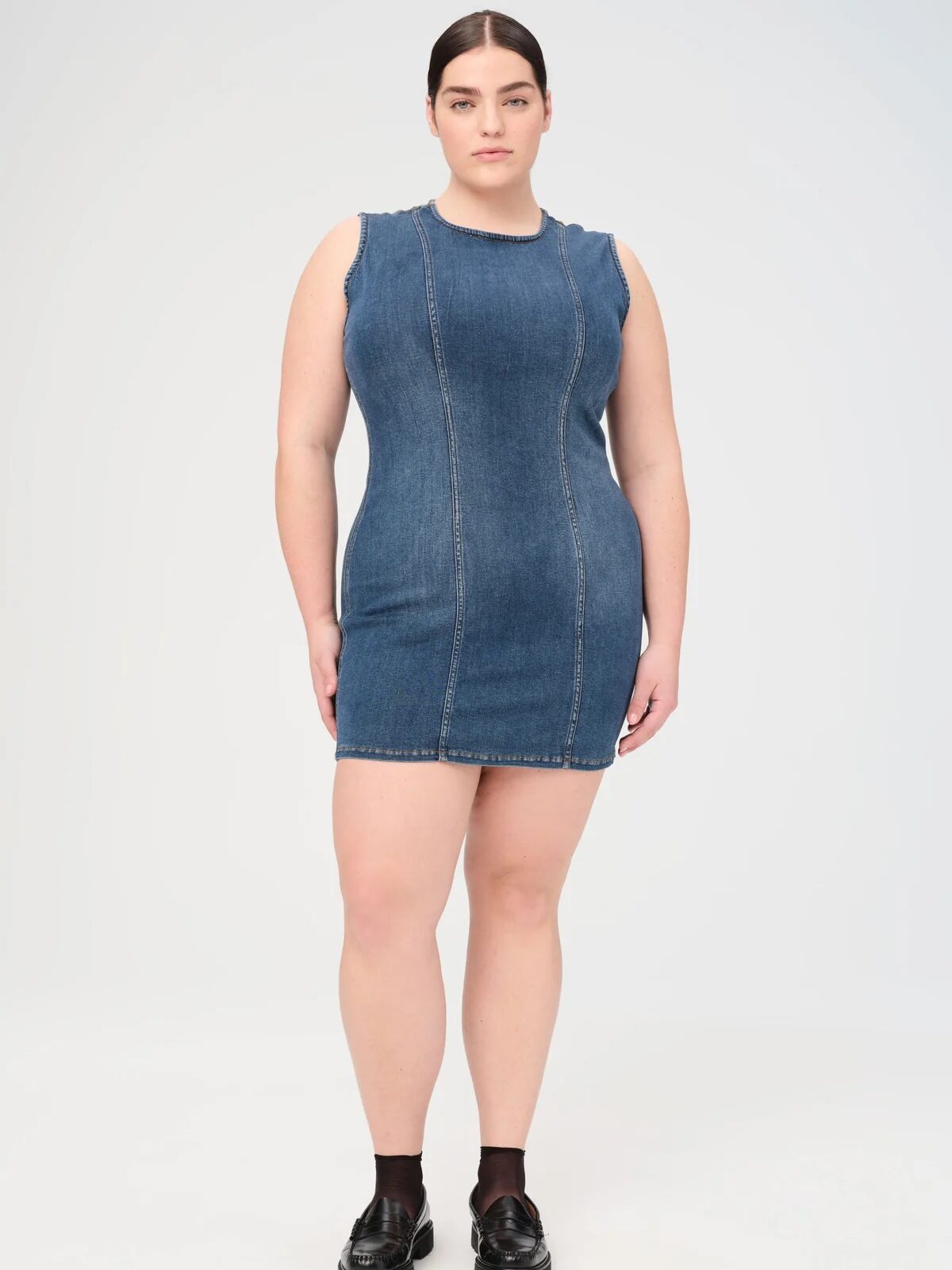 A plus size model wearing a denim dress from Warp + Weft. 