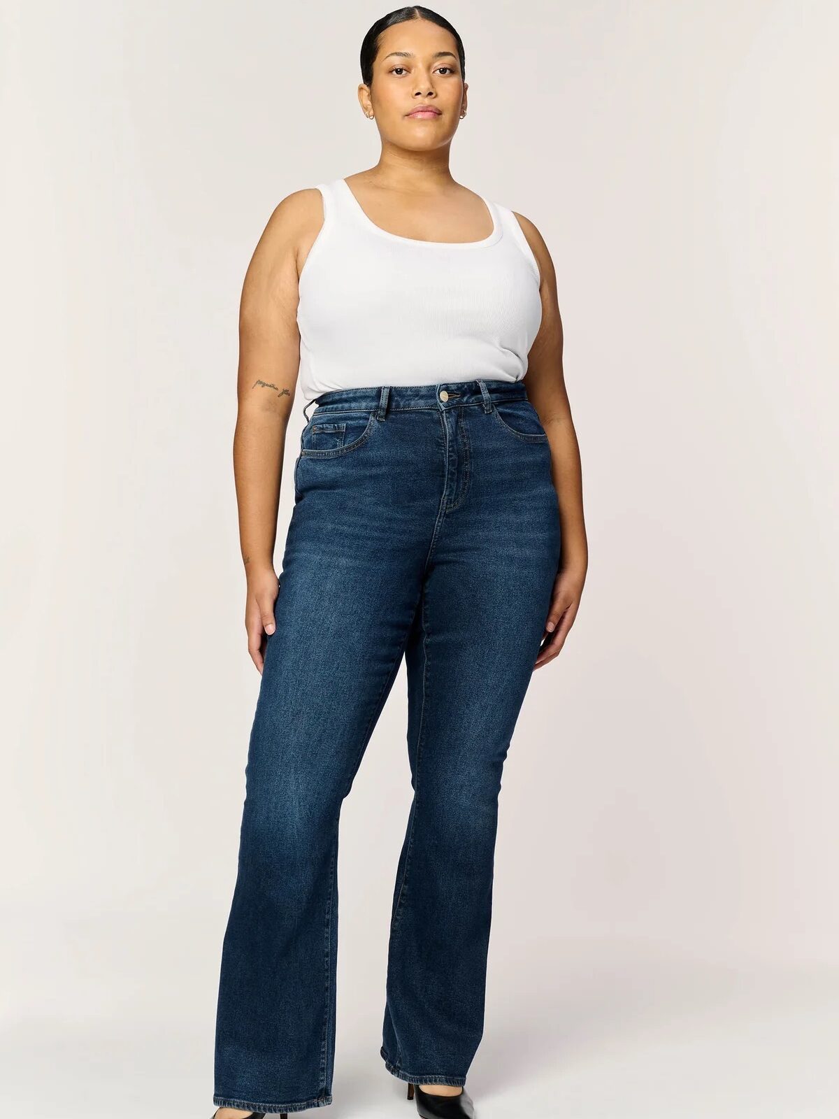 A plus size model wearing a pair of Warp + Weft bootcut jeans. 