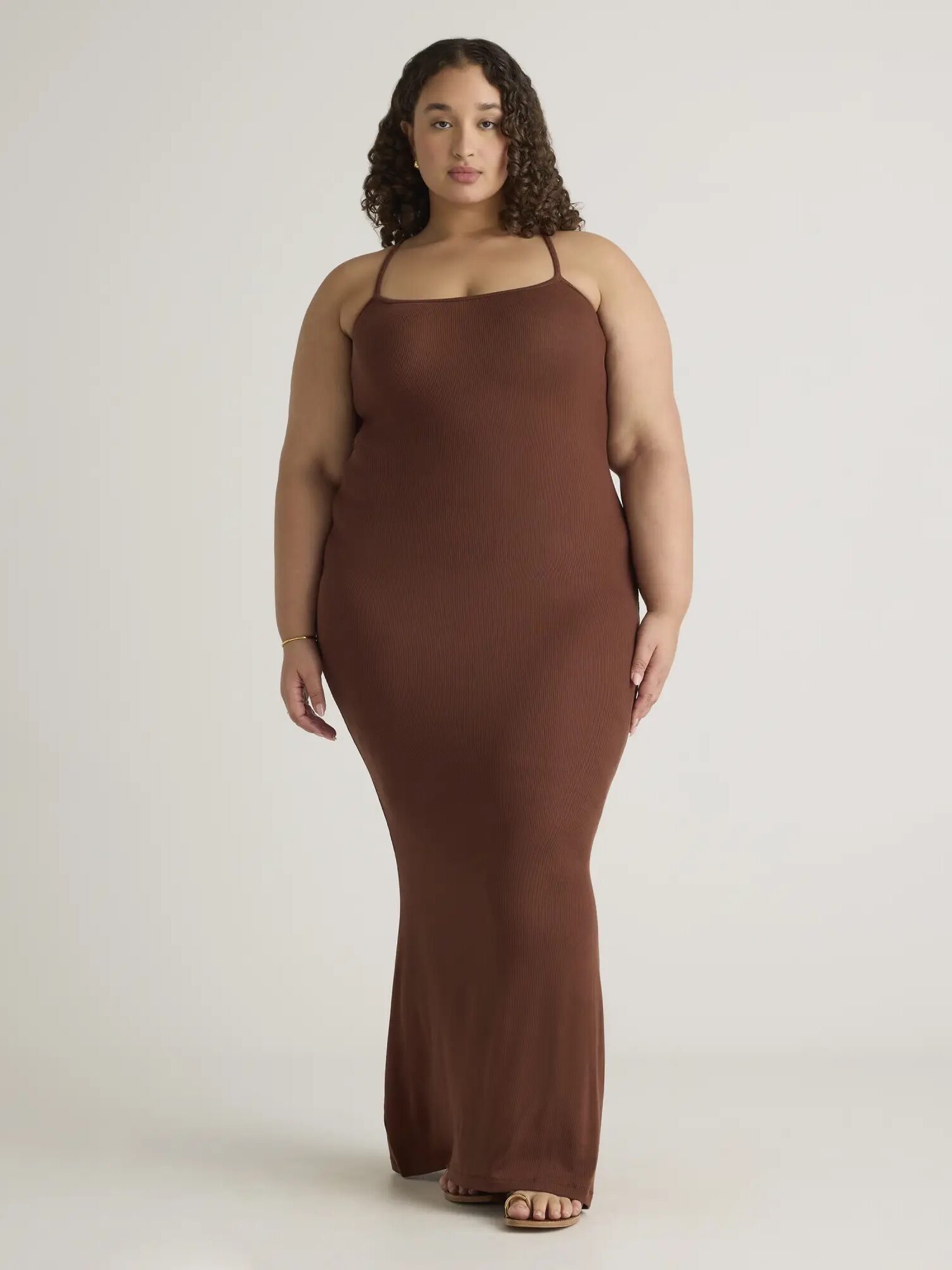 A plus size model wearing a brown slinky maxi dress from Quince. 