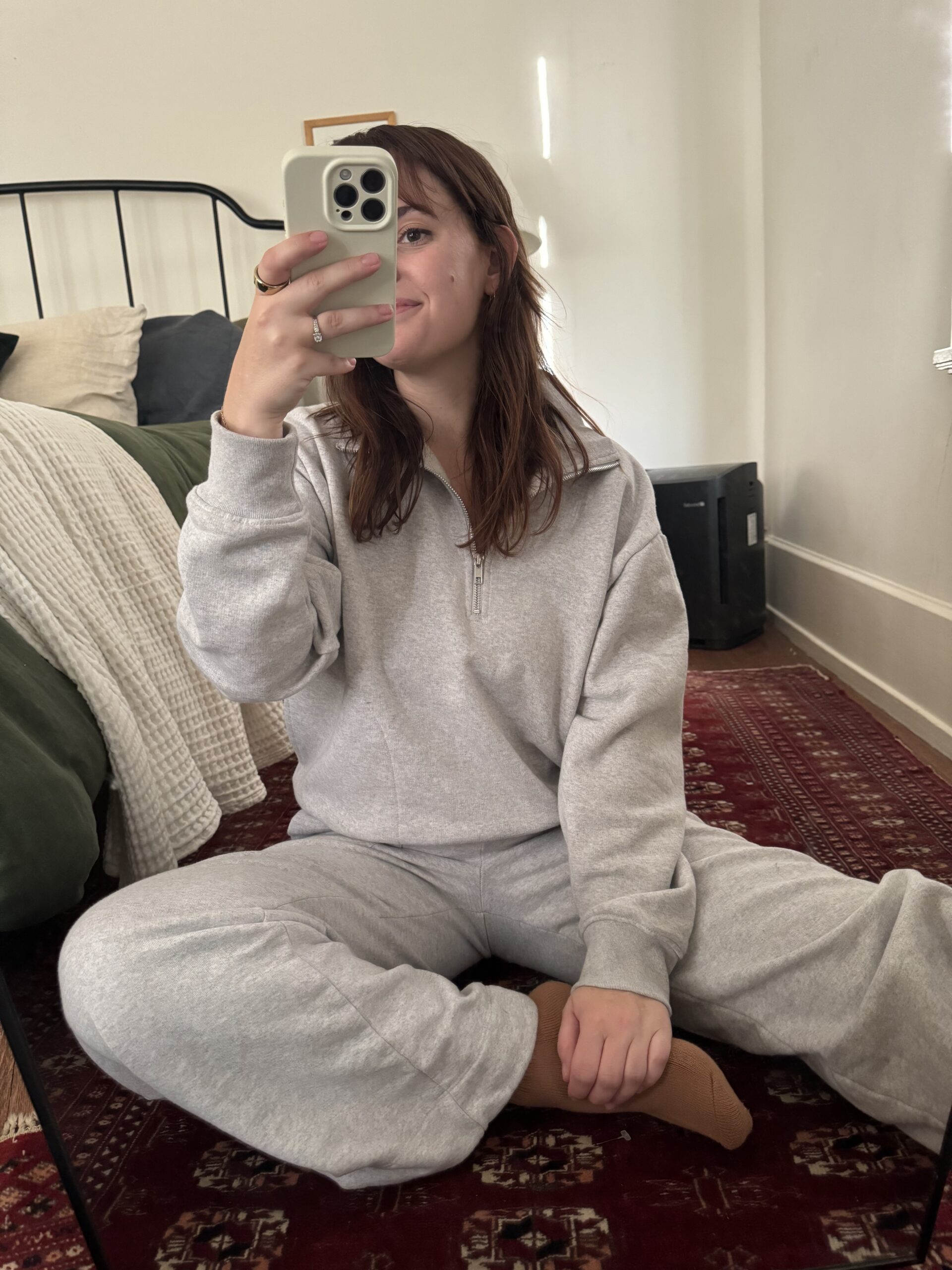 Kayti Christian, Senior Content Strategist at The Good Trade, wears a  heather grey long sleeve half-zip from MATE the Label, while taking a seated mirror selfie. 