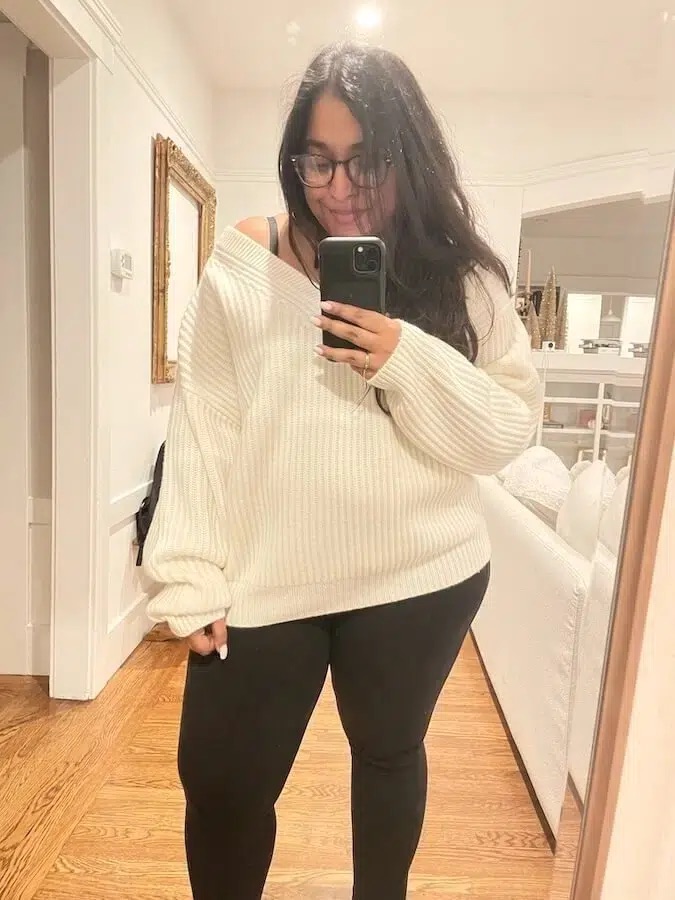 Henah Velez, Contributing Editor at The Good Trade, wears an oversized V-neck NAADAM sweater in white while taking a mirror selfie. 