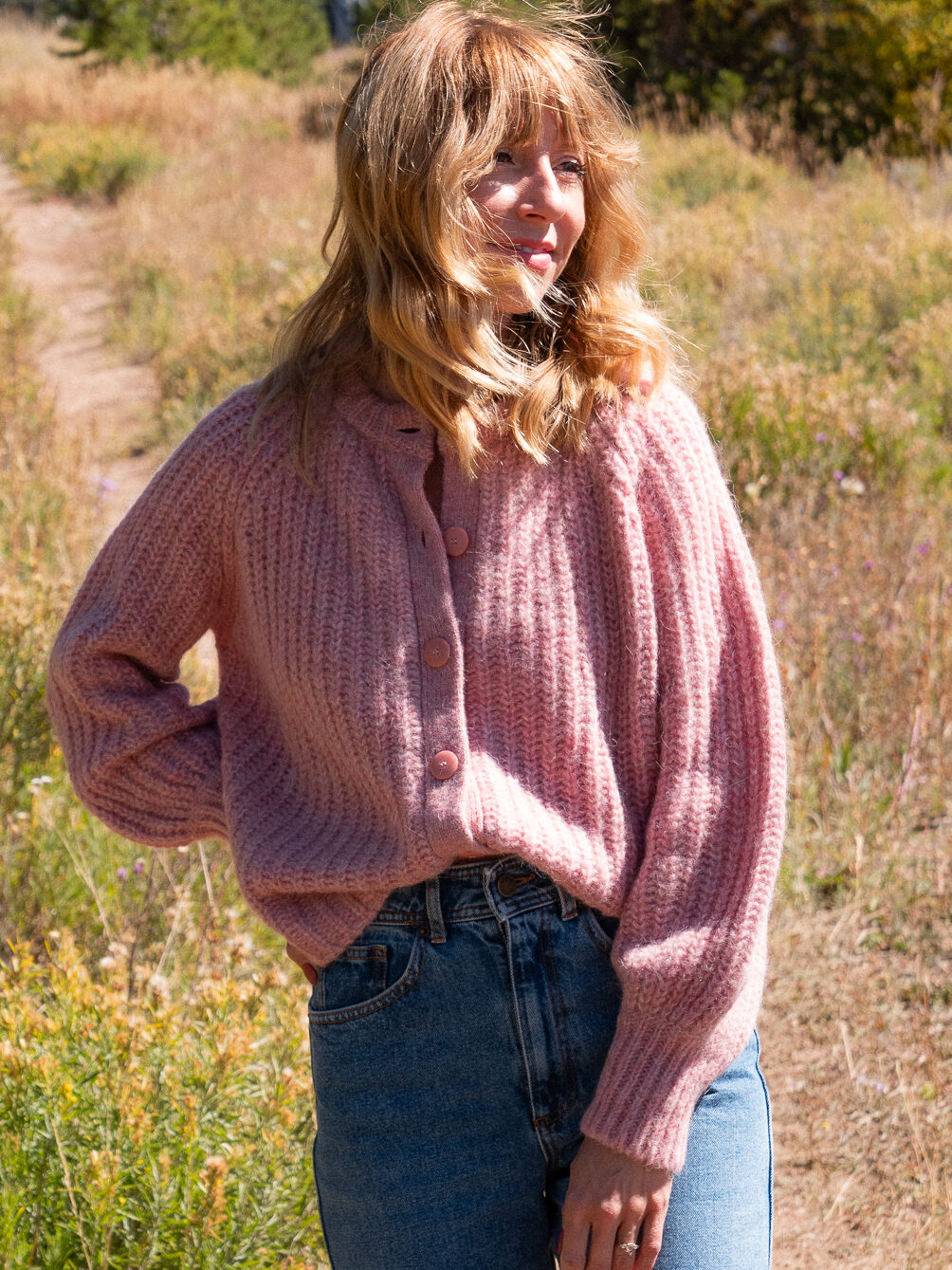 Courtney Jay Higgens, Contributing Editor at The Good Trade, wears a chunky pink button down cardigan from Sezane in a grassy setting. 